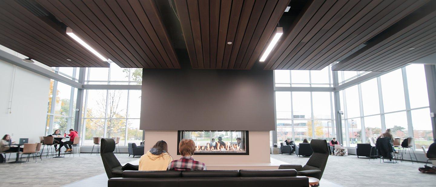 People seated on a couch looking towards a fireplace in the center of a large room.